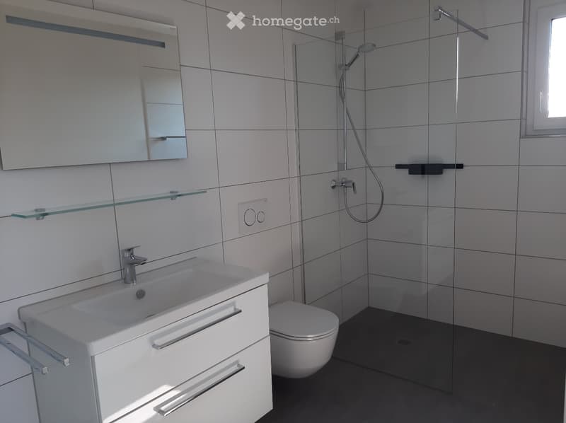 modern and spacious with white tiles, glass shower enclosure, silver faucet, white sink with drawers, recessed mirror, white toilet, and floor drain