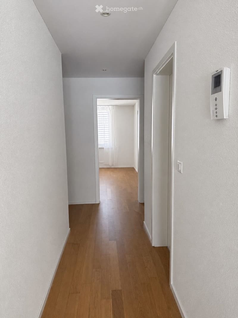 Empty hallway with light wooden flooring, white walls, and multiple doors leading to other rooms.