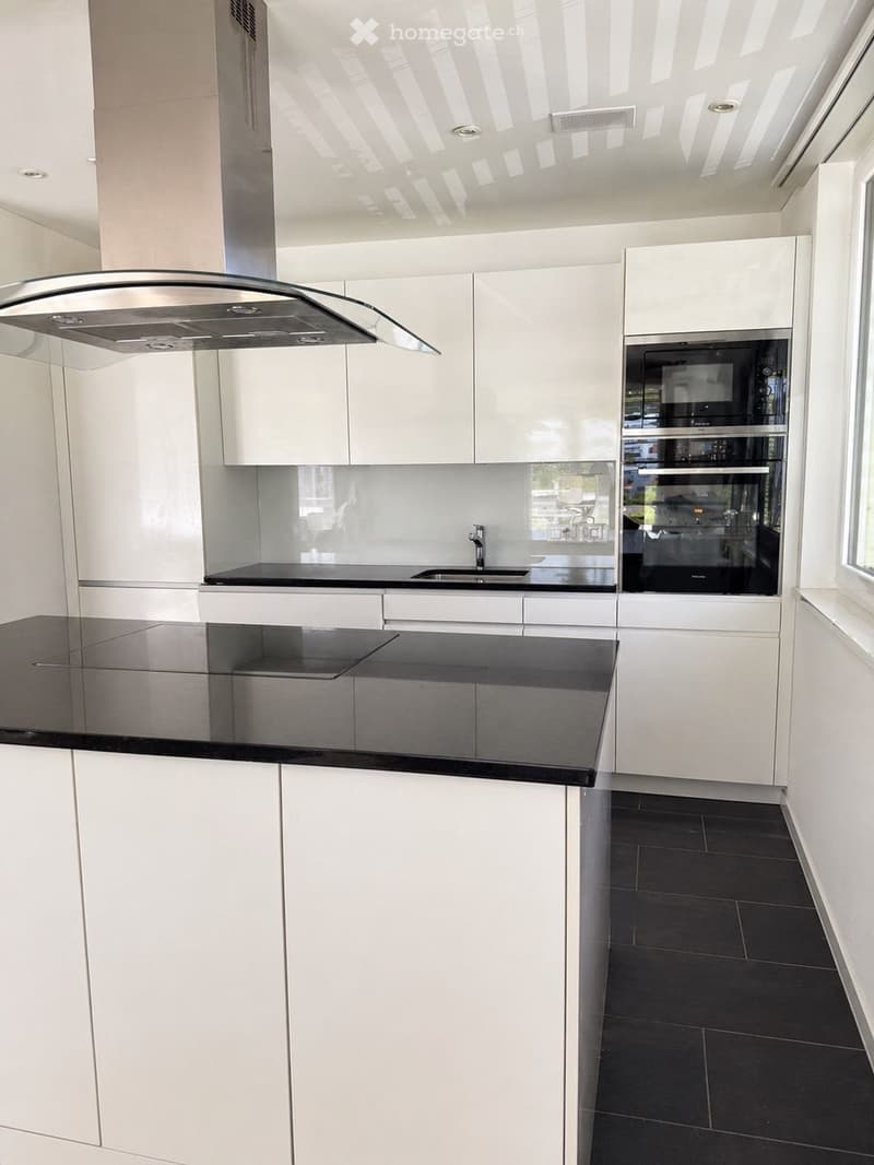 Modern kitchen with white cabinets, black countertops, and stainless steel appliances including a range hood and oven.