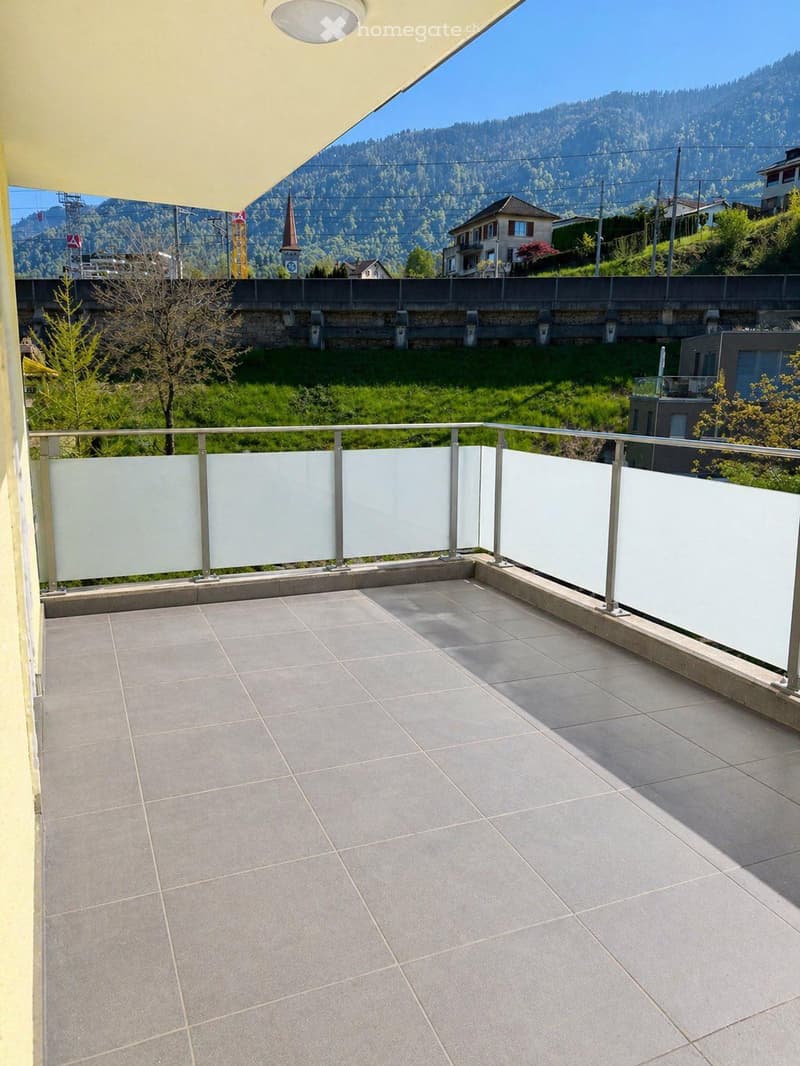 Balcony with tiled floor, white glass balustrade, and scenic mountain view in the background.