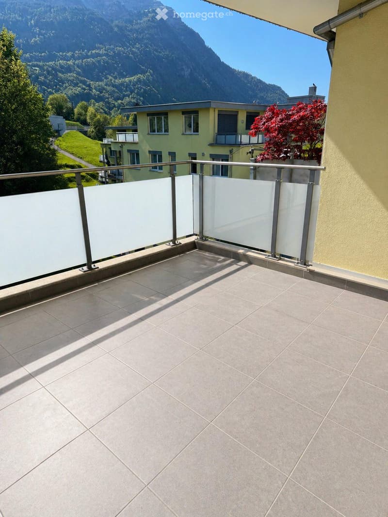 Balcony with tiled floor, glass railing, and scenic mountain view in the background.