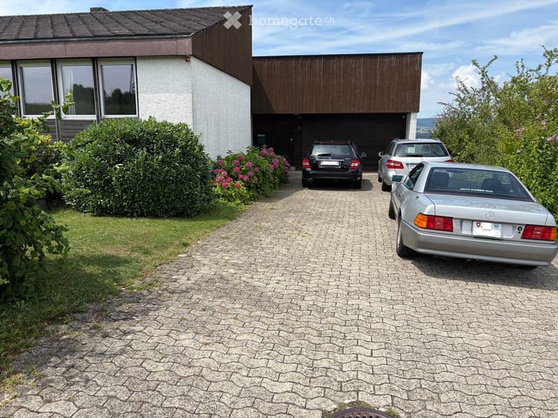 Front of house, driveway, brick house, bushes and flowers in front, garage with three cars parked in front