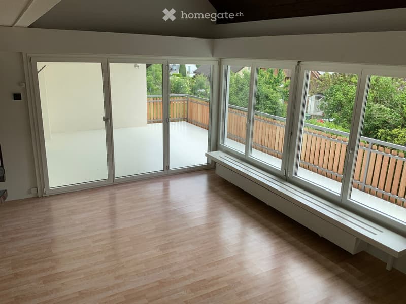 Empty room with wooden flooring, large windows, and sliding glass doors leading to a balcony.
