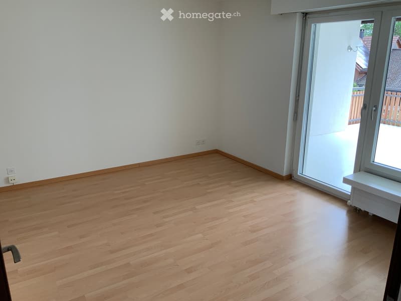 Empty room with light wooden flooring, white walls, and large sliding glass door leading to a balcony.
