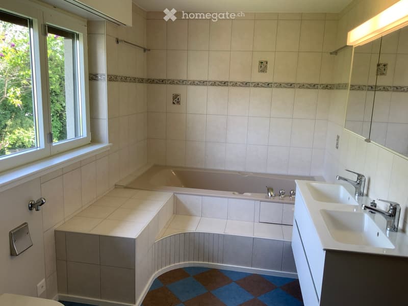 Modern bathroom with a large window, bathtub, double sink, and tiled walls.
