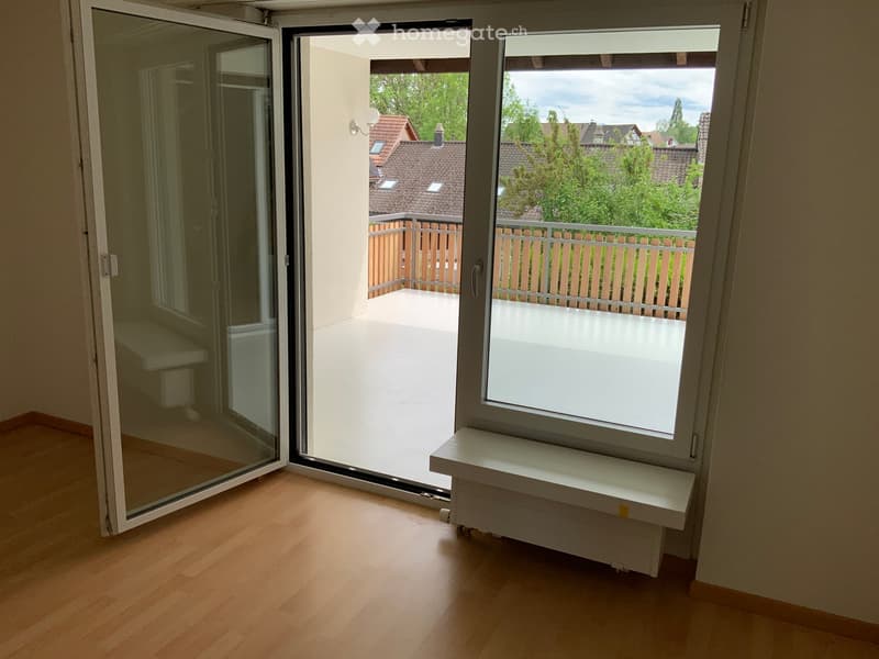 Empty room with wooden flooring, large sliding glass doors leading to a balcony, and a radiator under a window.