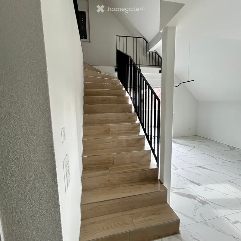 Modern staircase with wooden steps and a black metal railing, leading to an open area with marble flooring.
