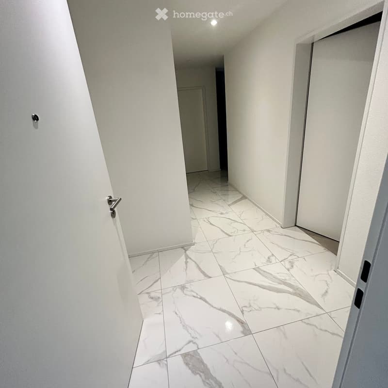 Clean, modern hallway with white marble tiles and white walls, featuring a central column and multiple doors.