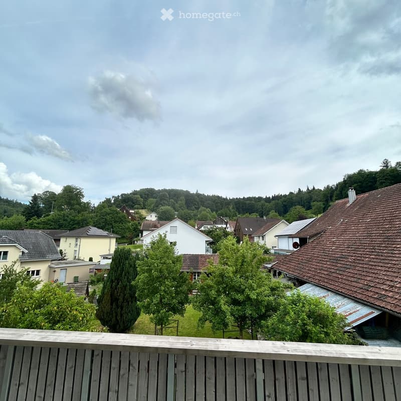 View from a wooden balcony overlooking a residential neighborhood with houses, trees, and a cloudy sky.