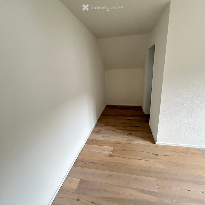 Empty room with light wooden flooring and white walls, featuring a doorway at the far end.
