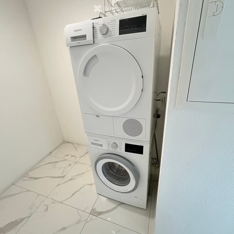 A small bathroom with a white washing machine and a white dishwasher stacked vertically, marble tiled floor, and white walls.