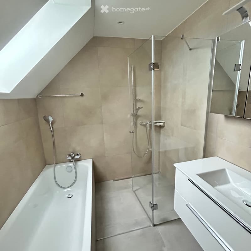 Modern bathroom with a bathtub, glass-enclosed shower, white sink, and mirror. Features beige tiles and a skylight window.