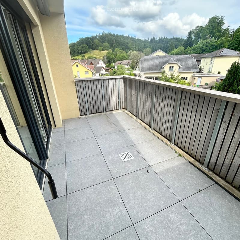 Balcony with grey tiled floor, wooden railing, and a view of a residential area with houses and greenery.