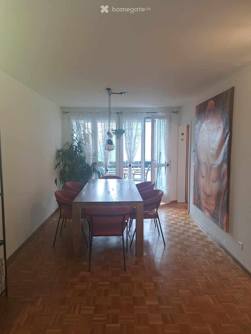 Dining room with wooden parquet flooring, a large wooden dining table surrounded by red chairs, a large painting on the wall, and a potted plant near the window.