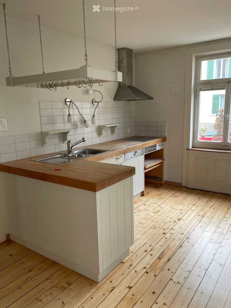 Modern kitchen with wooden countertop, sink, range hood, and built-in cabinets. Light-colored wooden flooring and white tiled backsplash.