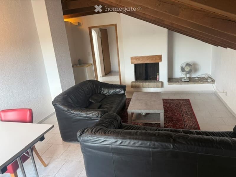 Living room with exposed wooden ceiling beams, fireplace, black leather sofa, coffee table, and fan on shelf.
