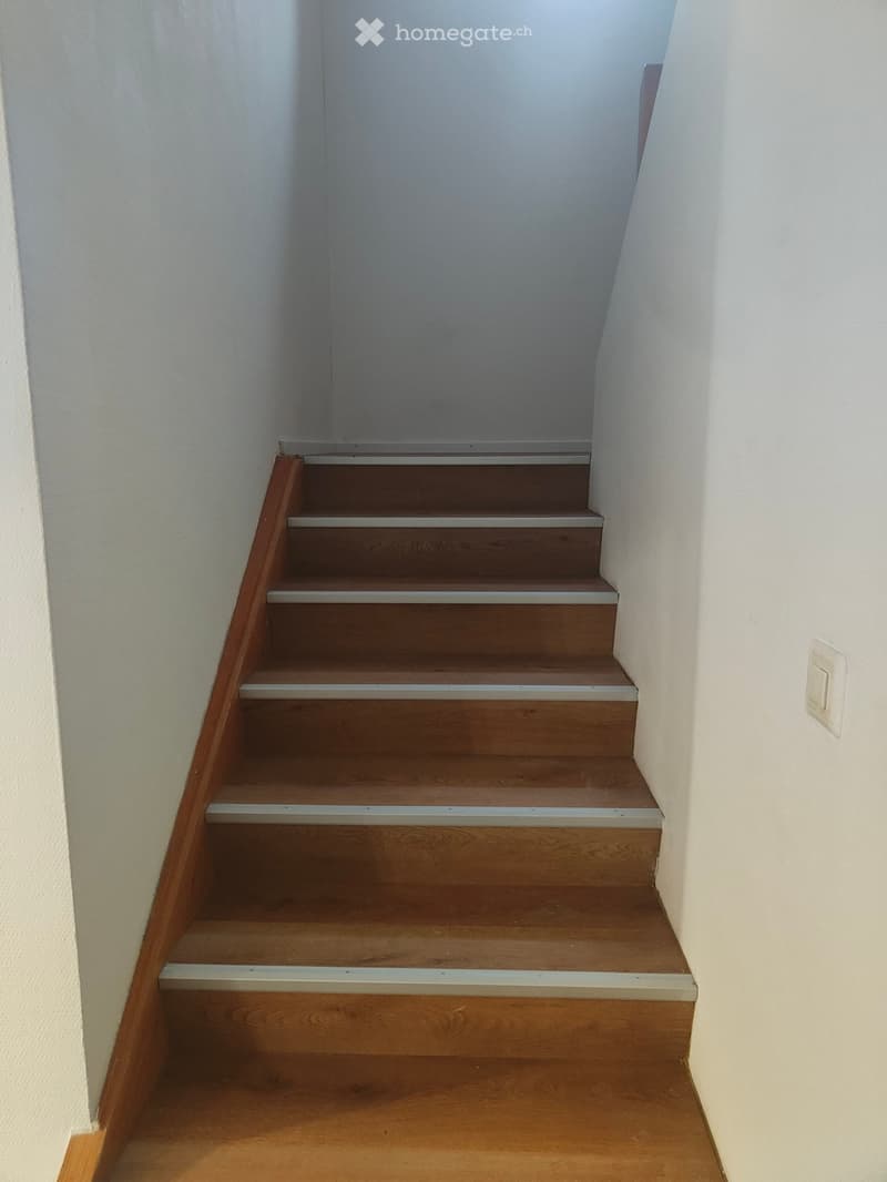 Wooden staircase with white walls and a light switch on the right side.