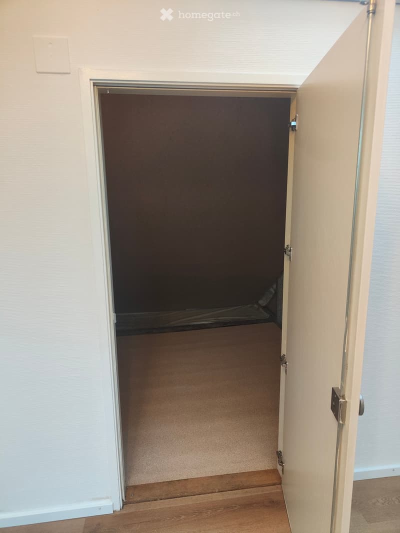 Open doorway leading to a dark room with wooden flooring and white walls.