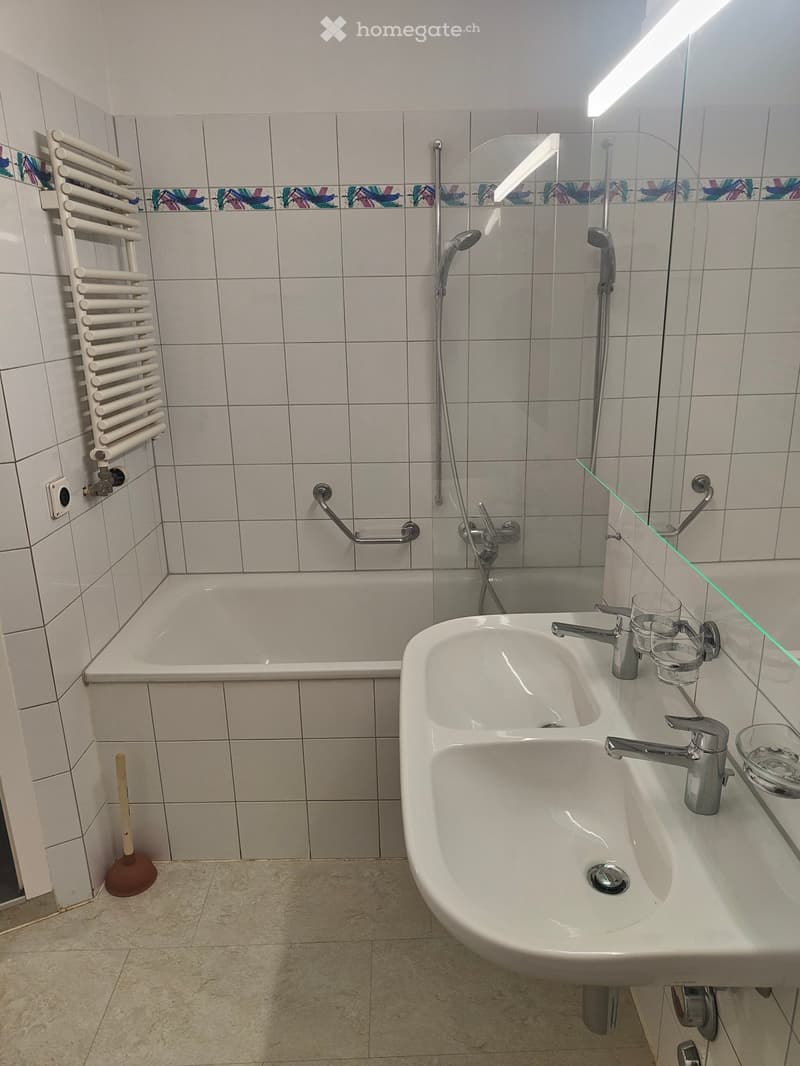 Bathroom with a bathtub, double sink, radiator, and a toilet brush on the floor.