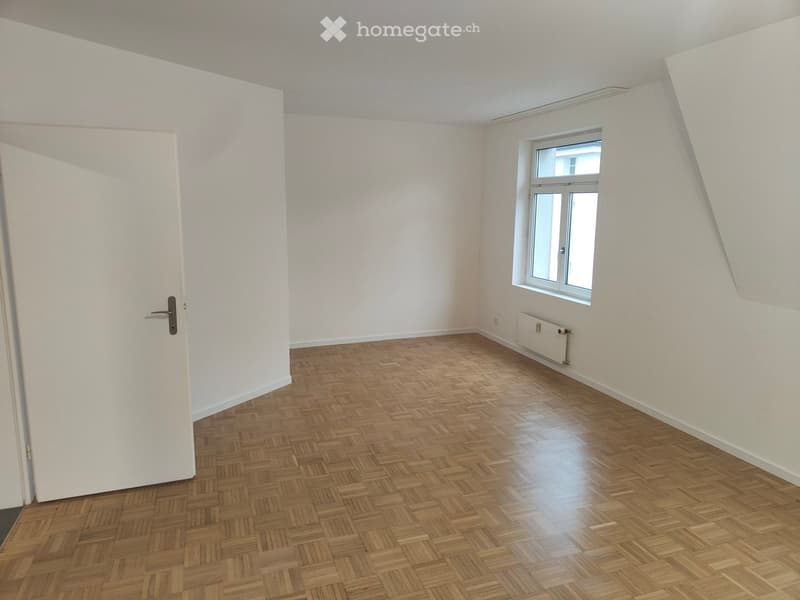 Empty room with wooden herringbone flooring, white walls, a single window, and a white door.