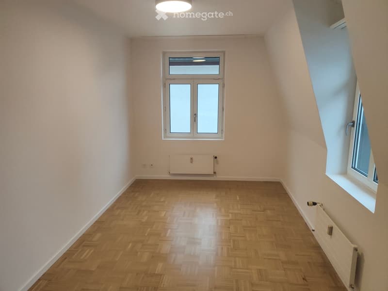 Empty room with wooden herringbone flooring, white walls, and two windows, one with a double door and the other a single window, both with frosted glass panels.