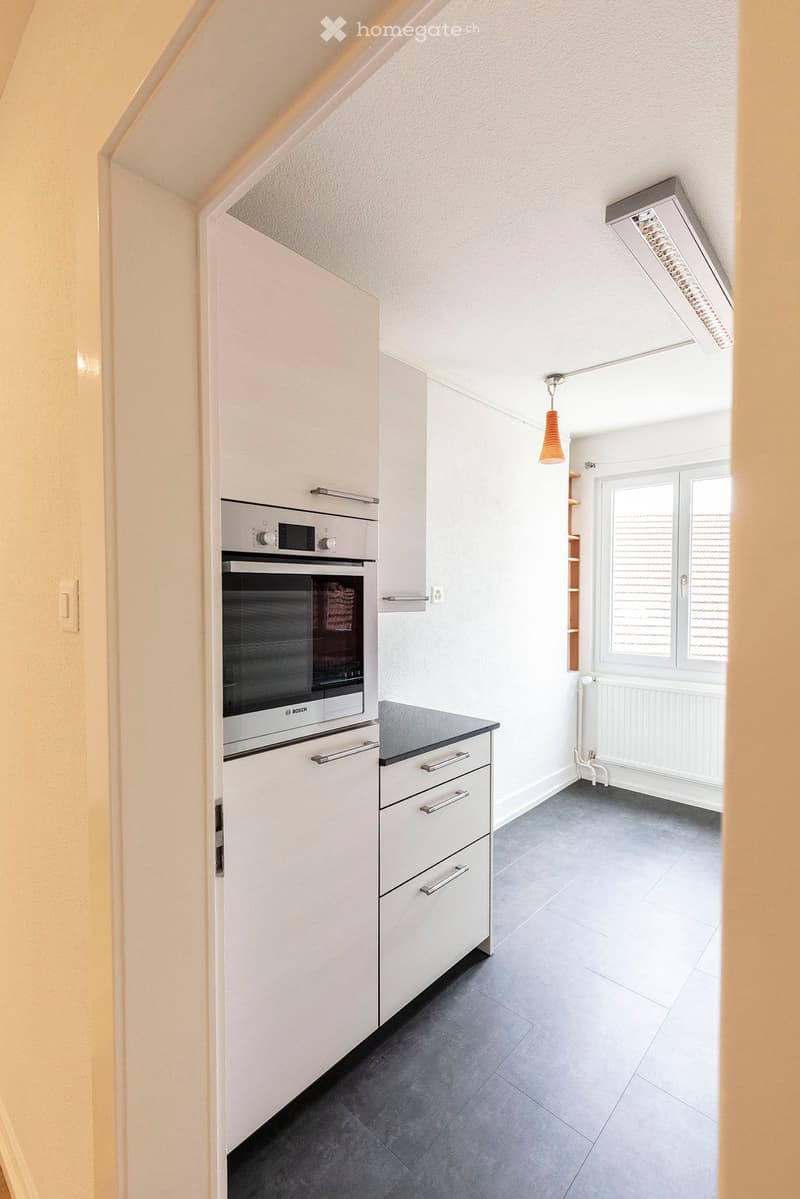 Modern kitchen with white cabinets, stainless steel oven, dark countertop, and grey tiled floor.