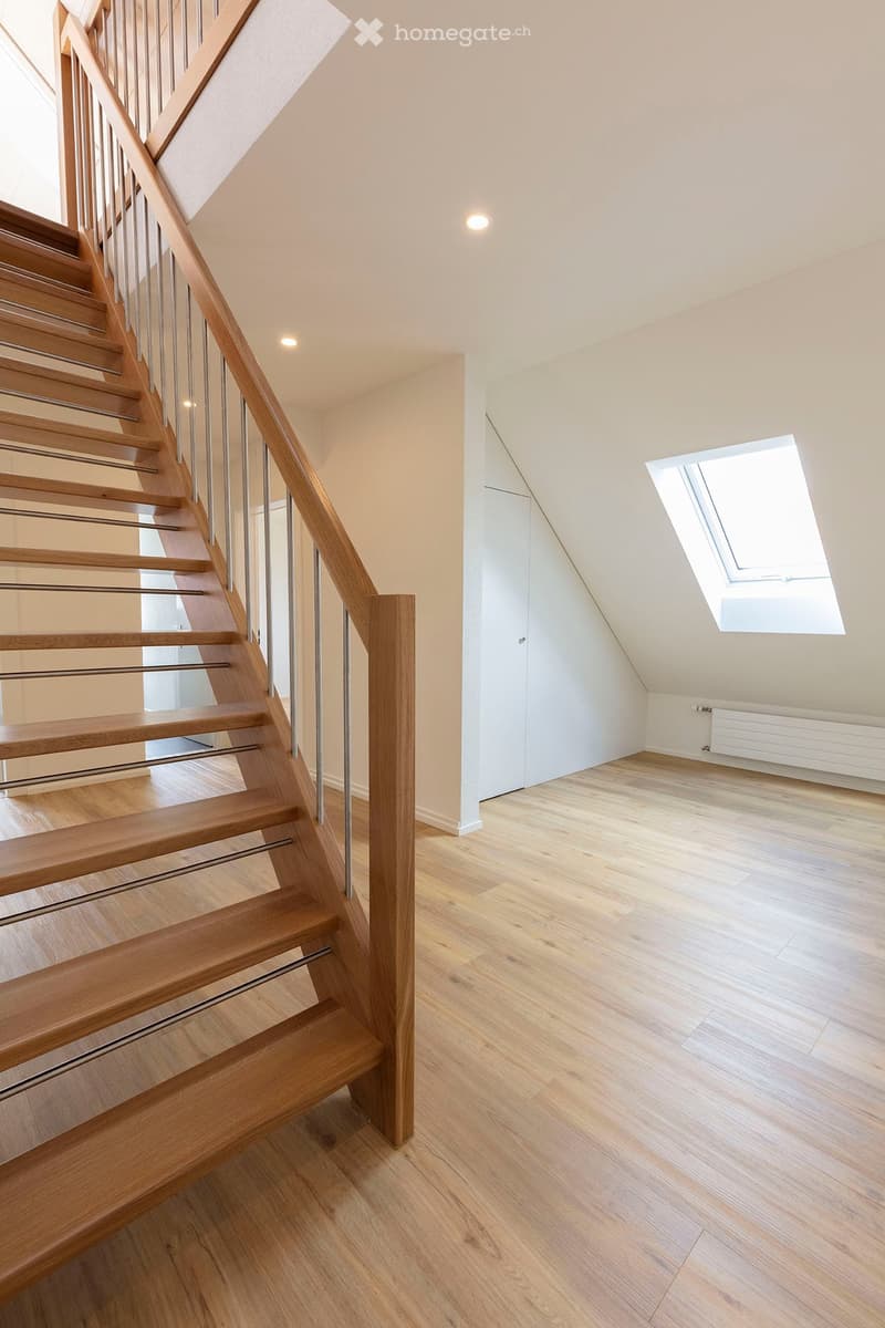 Modern hallway with wooden flooring, a wooden staircase with metal railings, and a skylight window providing natural light.