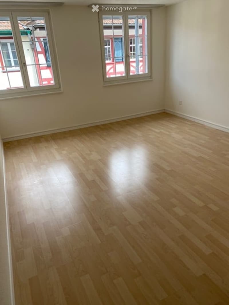 Empty room with light wooden flooring and large windows, no furniture or equipment.