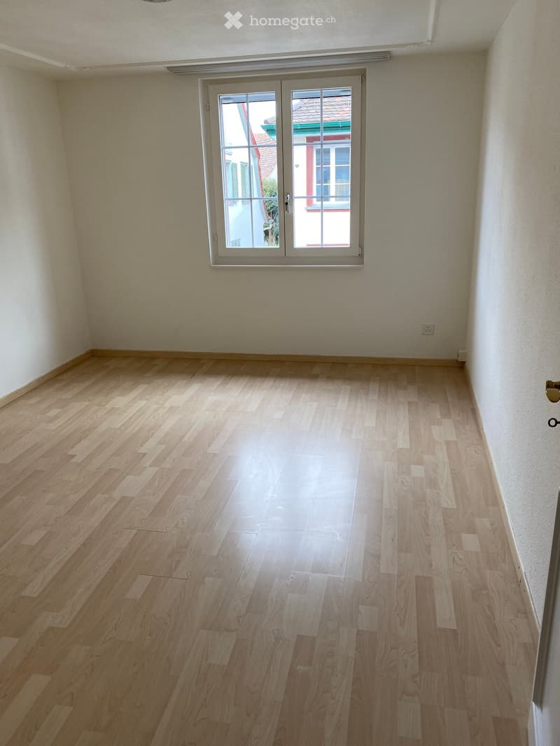 Empty room with light wooden flooring and white walls, featuring a large sliding glass door leading outside.