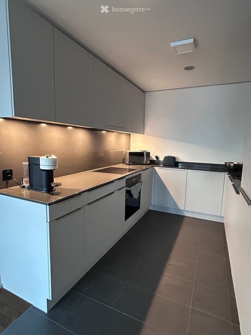 Modern kitchen with white cabinets, dark countertops, and stainless steel appliances including a coffee machine, microwave, and oven.