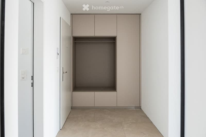 Empty hallway with built-in closet featuring closed doors and a small open shelf, light-colored walls, and tiled floor.