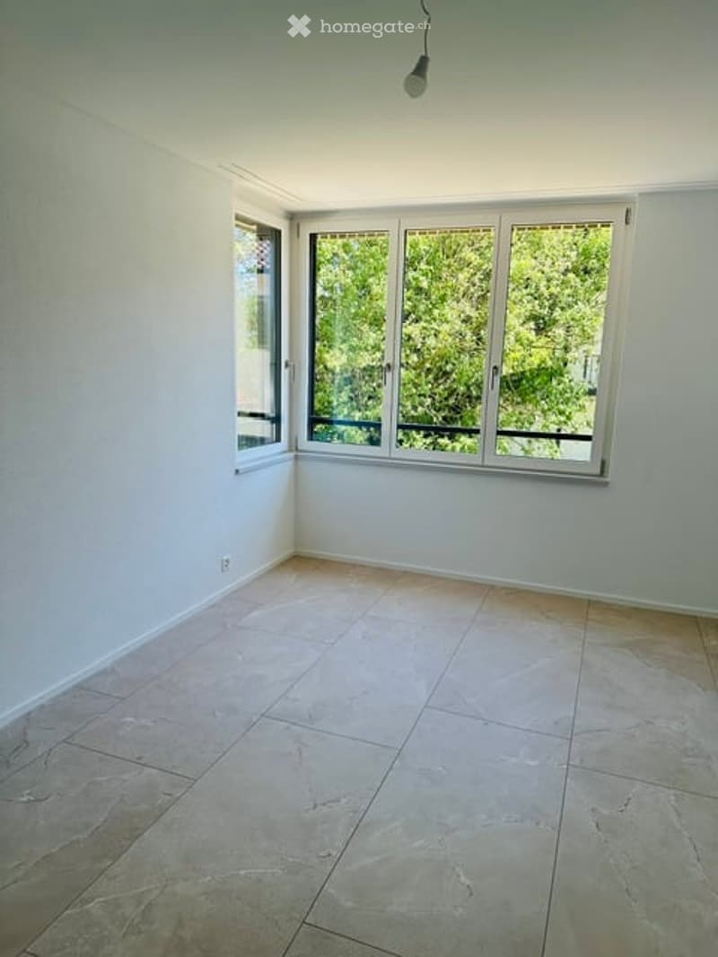 Empty room with light-colored tiled flooring, white walls, and large windows with white frames and blinds, allowing natural light to fill the space.