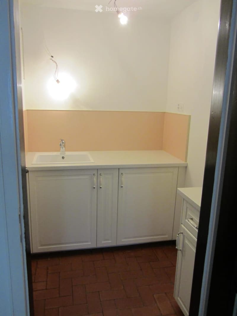 A small kitchen with white cabinets, a sink, and a tiled floor.