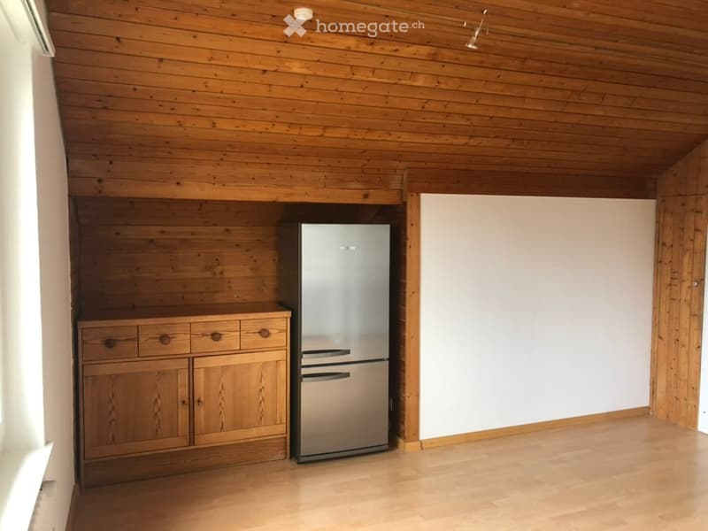 A small kitchen area with wooden walls and ceiling, featuring a stainless steel refrigerator and wooden cabinets.