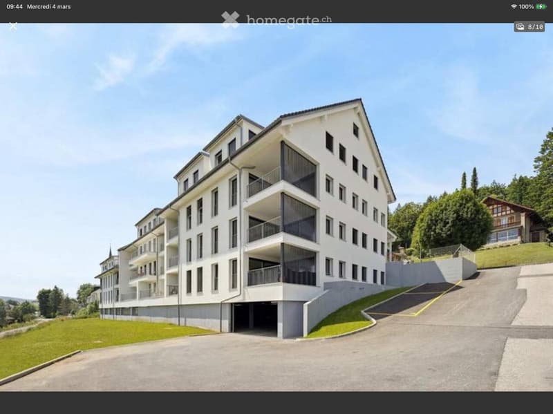 Modern apartment building with multiple floors, balconies, and a garage entrance.