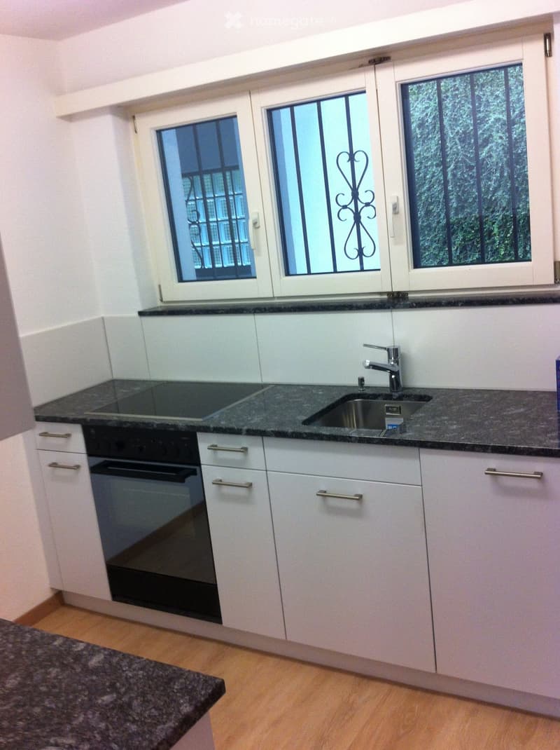 Modern kitchen with white cabinets, granite countertops, a sink with a faucet, and an oven. The room has large windows with decorative grilles.