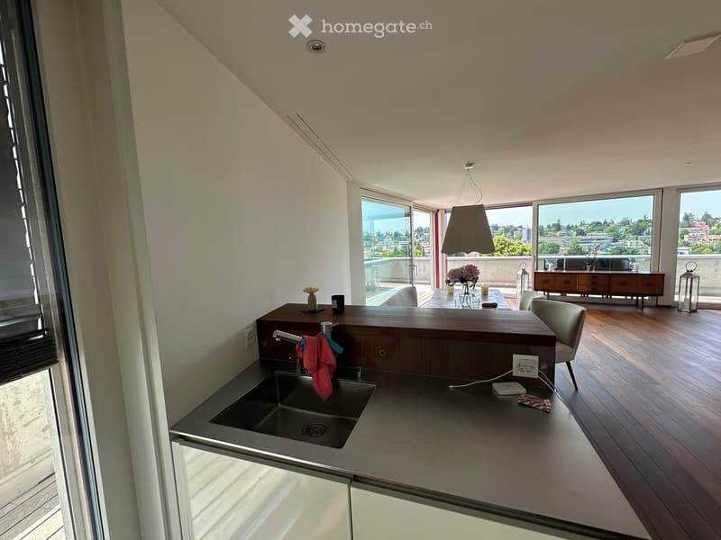 Modern kitchen with stainless steel sink, wooden countertop, and large windows offering a scenic view. Includes a dining area with a table and chairs.