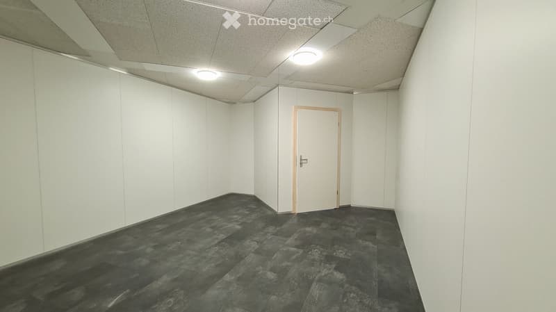 Empty room with white walls, gray tile flooring, and a single door. The room has recessed lighting in the ceiling.