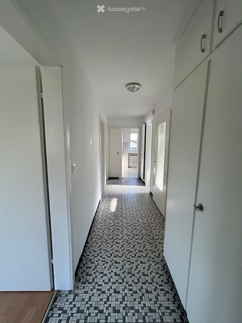 Empty hallway with white walls, tiled floor, and several doors leading to rooms.