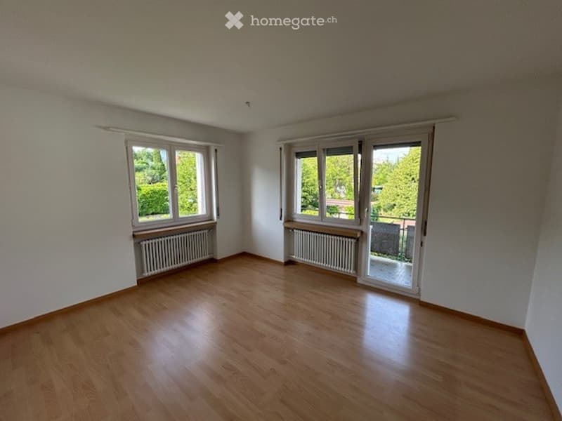 Empty room with wooden flooring, white walls, large windows, and radiators. No furniture or equipment present.