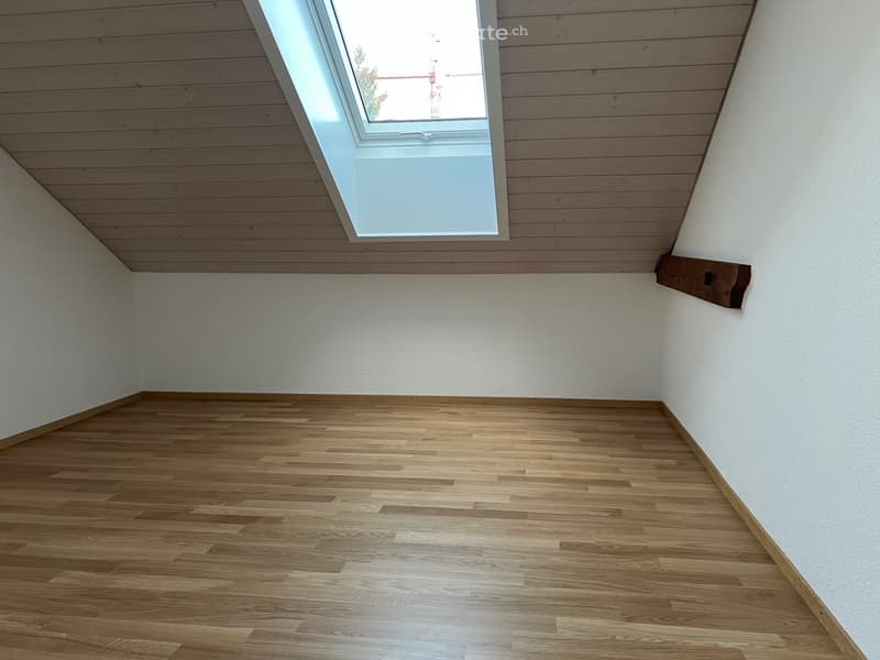 Empty room with wooden flooring, white walls, and a skylight window allowing natural light.