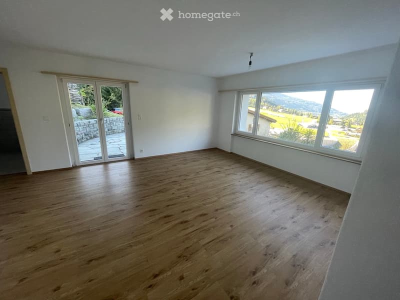 Empty room with wooden flooring, large windows, and a sliding glass door leading to an outdoor area.