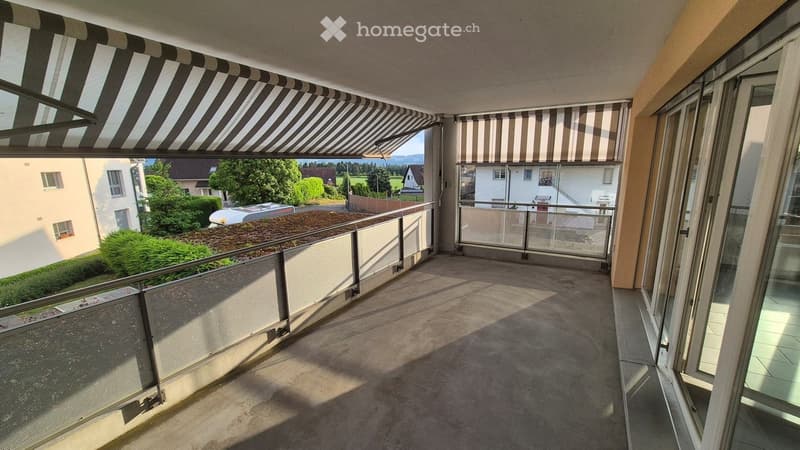 Balcony with striped awning, metal railing, and view of the surrounding area and greenery.