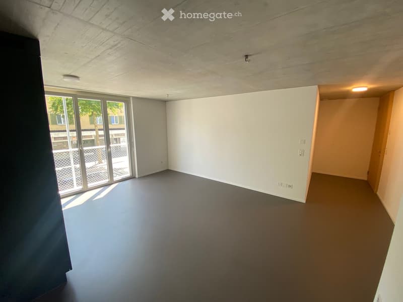 Empty room with white walls, dark grey floor, large sliding glass door leading outside, and recessed lighting.