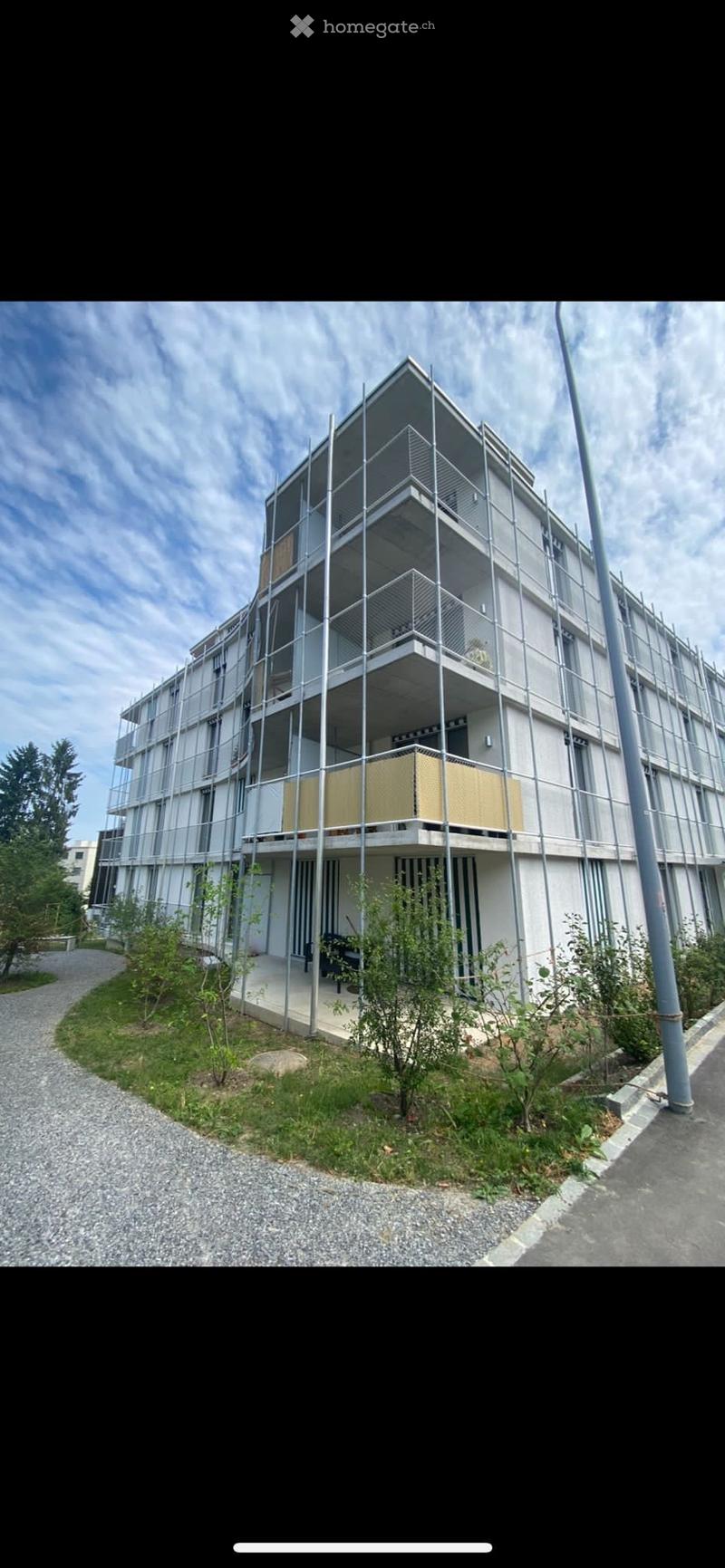 Modern multi-story building under construction with scaffolding, balconies, and a partially visible yellow panel on one balcony.