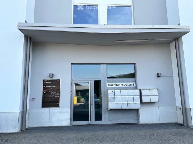 Modern building entrance with glass doors, mailboxes, and signage for 'Eisenbahnstrasse 5'.