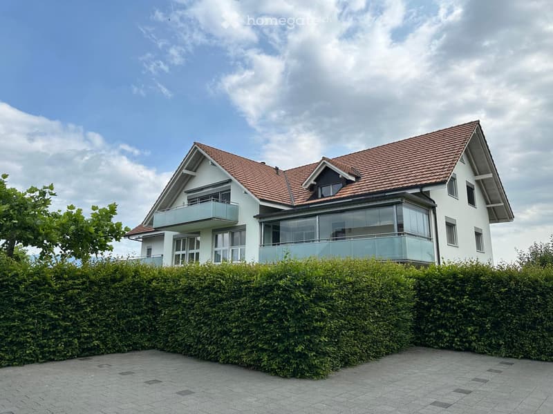 Modern two-story house with white exterior, red-tiled roof, large windows, and a balcony on the upper level.