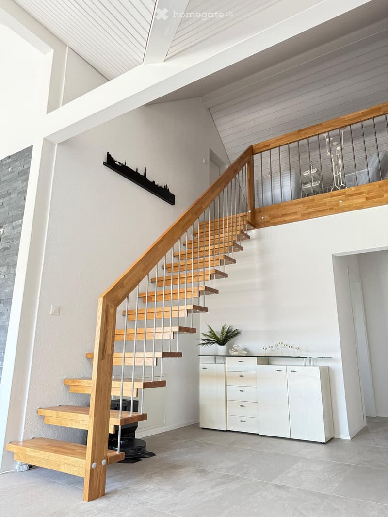 Modern hallway with a wooden staircase featuring metal railings, white cabinetry, and a small plant on the counter.