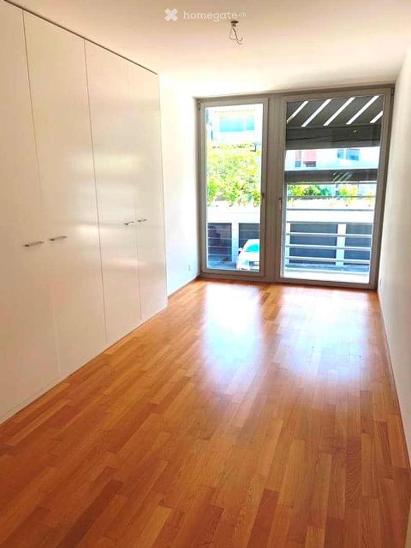 Empty room with wooden flooring, white walls, large sliding glass doors leading to a balcony, and built-in white closet units.