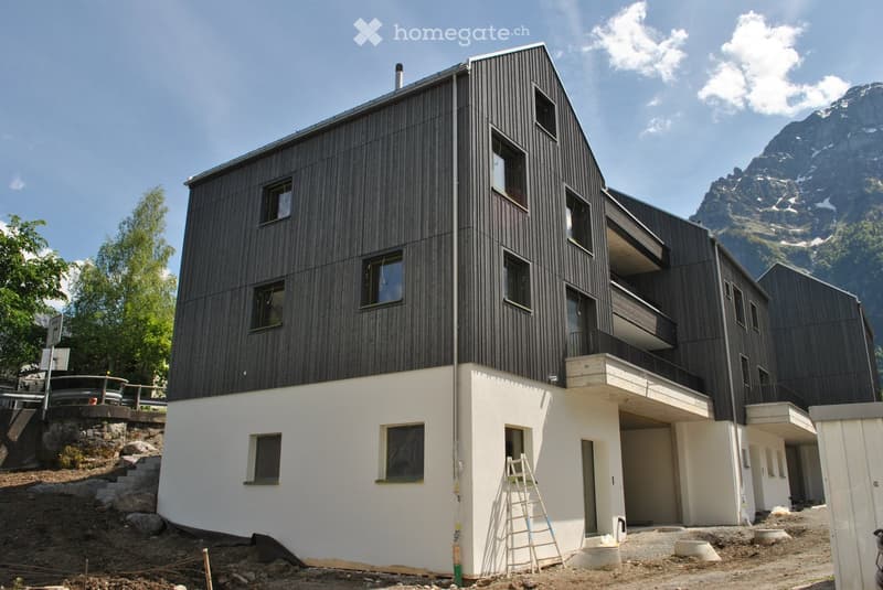 Modern two-story building with dark wooden facade and white lower level, featuring multiple windows and a raised ground floor.